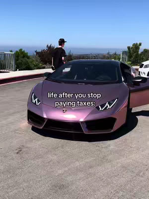 A man stands next to a purple sports car with the door open. Behind him is a scenic background of trees under a blue sky.