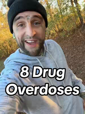 A selfie-style shot features a man at a slight angle, with the background blurred, possibly outdoors, with foliage and filtered sunlight. He sports a black beanie, tattoos, and a gray hoodie, looking directly at the camera and smiling. The text overlay reads "8 Drug Overdoses" in large, bold, white letters.