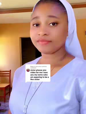 A woman in a white head covering, dressed in a white outfit, is looking at the camera. A text overlay shows a comment on the image. The background is a simple setting with warm-toned walls and a wooden chair in the background.