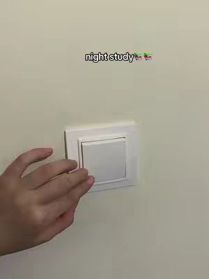 A hand reaches towards a white light switch on a light beige wall. Above the switch, there is text in black.