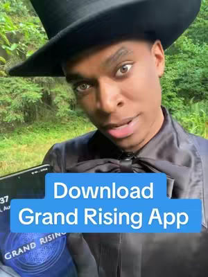 A man in a black hat and suit stands in front of a blurred green background. A text overlay in a blue box reads, Download Grand Rising App.