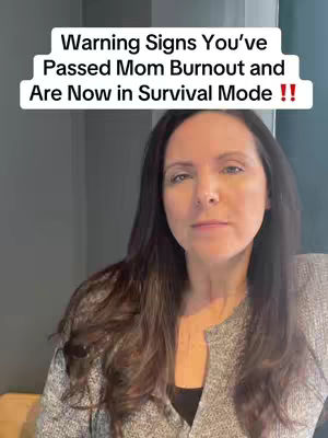 A woman with long brown hair and a gray sweater is centered in the frame. Above her head, a white bar displays the text "Warning Signs You've Passed Mom Burnout and Are Now in Survival Mode !!". The background is a plain gray wall.