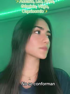 A young woman is captured in a medium shot, looking slightly to the side with a neutral expression. The background is an evenly lit, muted green. Above her head, a strip of bright green light adds a contrast color. Text overlays the image, with sections in white font and green glitter, listing zodiac signs.
