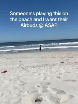 A serene beach scene under a clear blue sky, with white sand in the foreground and ocean waves in the background. A person is seen walking along the waterline in the distance, and text overlay adds context to the environment.