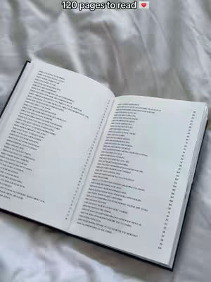 An open book lies on a white surface, likely a bed, with pages filled with text visible. The cover of the book is black, providing contrast to the white pages. The composition is simple, focused on the book, and suggests a personal or intimate context.