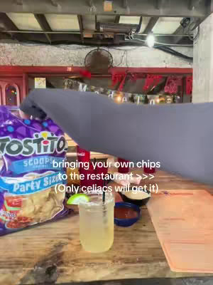 A hand holding a bag of tortilla chips next to a margarita glass on a wooden surface. Text overlays describe the situation.