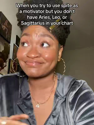 A woman with dark skin and afro-textured hair is the main focus. She's wearing a gray velour zipped jacket and gold jewelry, including hoop earrings and a necklace with a Libra pendant. The background is a room, with wall art. The text overlay describes an astrology-related sentiment.