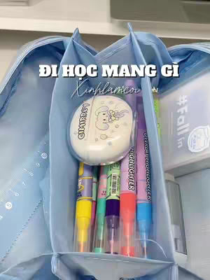 The image shows a light blue pencil case open to reveal its contents. Inside are various colorful highlighters, a white round object with a cartoon image, and other stationery items. The composition is well-lit, and the items are neatly arranged.