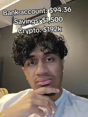 A selfie-style image features a young man with short, curly black hair, looking at the camera with a thoughtful expression. Above his head, text overlays display financial information: 'Bank account: $94.36', 'Savings: $1,500', and 'Crypto: $192k', framed by a portion of a white, modern-style ceiling fixture.