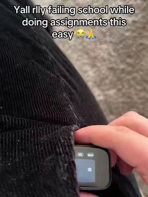 A person's hand is reaching into the pocket of black corduroy pants, retrieving a small, black rectangular device with a screen.
