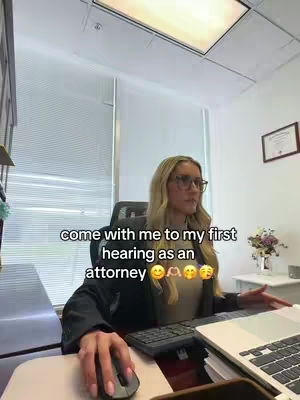 A woman with blonde hair and glasses is seated at a desk in an office setting, using a laptop and mouse. Text overlayed on the image reads, 'come with me to my first hearing as an attorney'.