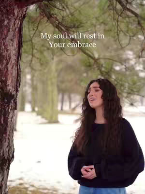 A young woman with long, dark curly hair is singing outdoors in a snowy setting. Text overlayed indicates lyrics.