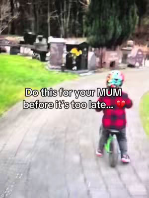 A child riding a green bicycle on a paved path in a cemetery. The child wears a colorful helmet and a red and black plaid shirt. The path leads towards gravestones and trees in the background. Text overlays the image.