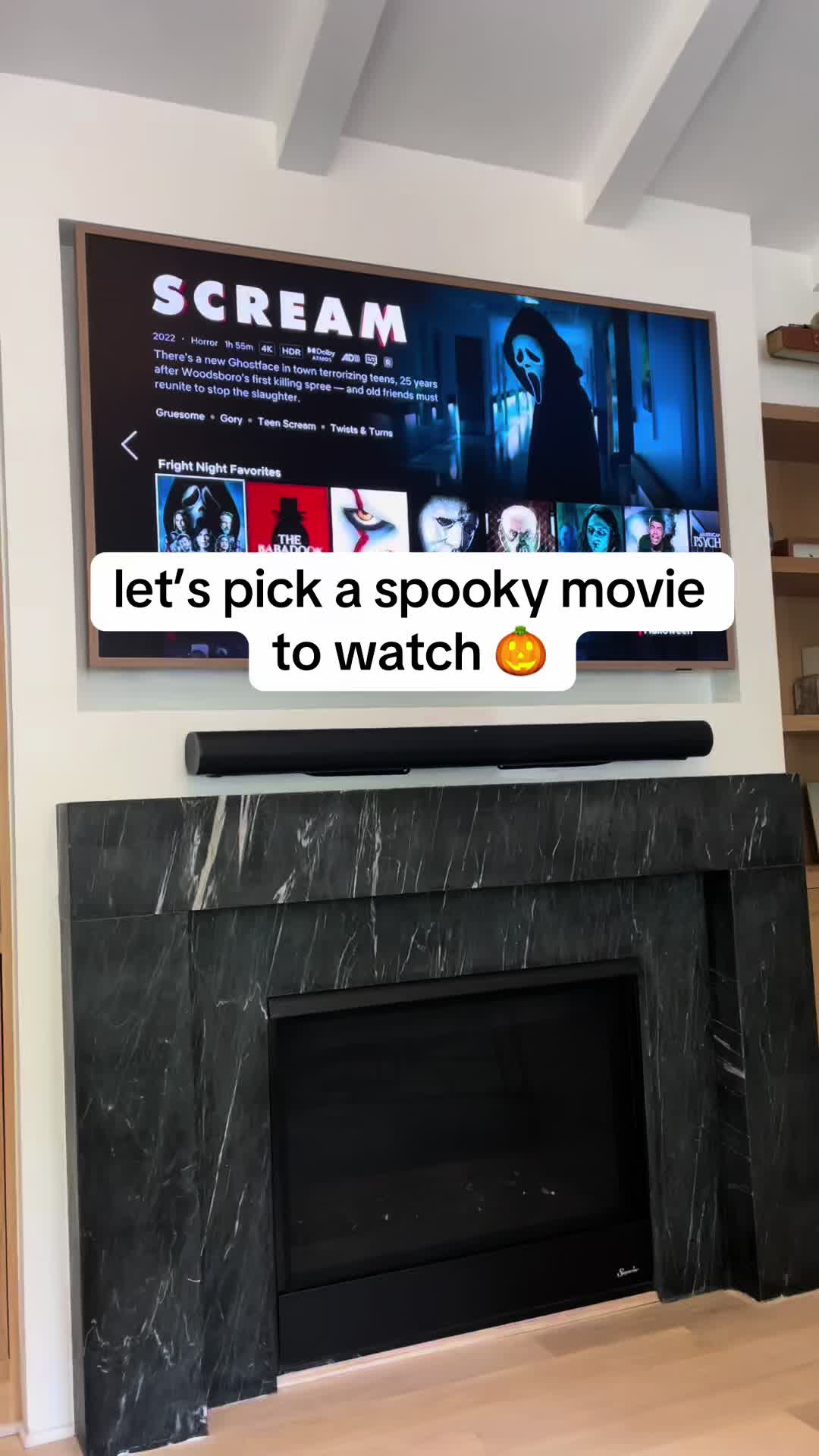 A person has a show on a TV that is turned on, advertising the movie 'Scream'. A white oval-shaped box is displayed on top of the TV screen with the words: 'let's pick a spooky movie to watch' and next to it is a pumpkin emoji.