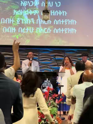 The cover image captures a scene from what looks like a church service. A man and a woman are standing on the stage, holding microphones and speaking. The background features a large screen displaying text, and the overall tone appears to be religious or spiritual. Audience members can be seen in the foreground.