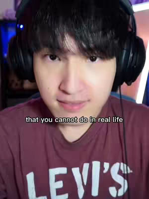 A young man with dark hair and headphones looks directly at the camera with a slight smile. He's wearing a maroon shirt with a white logo, likely a brand. Text overlayed on the image reads, "that you cannot do in real life". The background is blurry, suggesting an interior setting, possibly a gaming space.