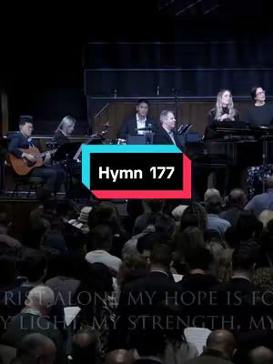 The cover image shows a church choir and orchestra performing on a stage. The front of the stage fills with seated people, likely the congregation. The caption text overlays the bottom of the image within the body. The title is in a box in the center of the screen with the black text and a white background outlined in red and blue.