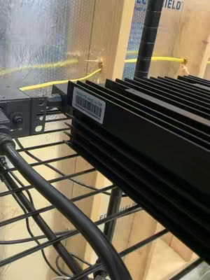 The cover image presents a close up view of a black Kaspa miner resting on a wire rack with other machine parts. The miner has a label. The background includes insulated walls and some wooden support.