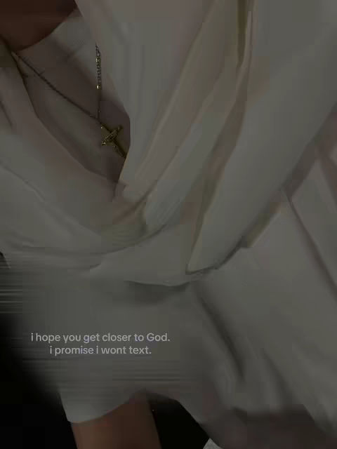 The image features a person, the top of their body covered in white fabric. A gold cross necklace hangs from their neck. Text overlayed in lower-case white letters is placed below.