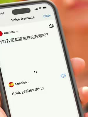 The image is a close-up of a smartphone screen displaying a voice translation app. The screen has two sections, showing translation between Chinese and Spanish. Part of the phone is held, and the background is blurred, suggesting a natural outdoor setting.