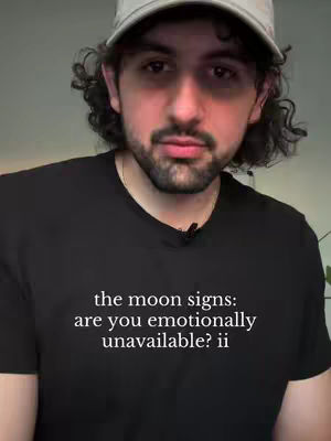 A man wearing a black shirt and a baseball cap looks directly at the camera. The text overlay on the shirt reads, "the moon signs: are you emotionally unavailable? ii". The background is a simple, blurred indoor setting.