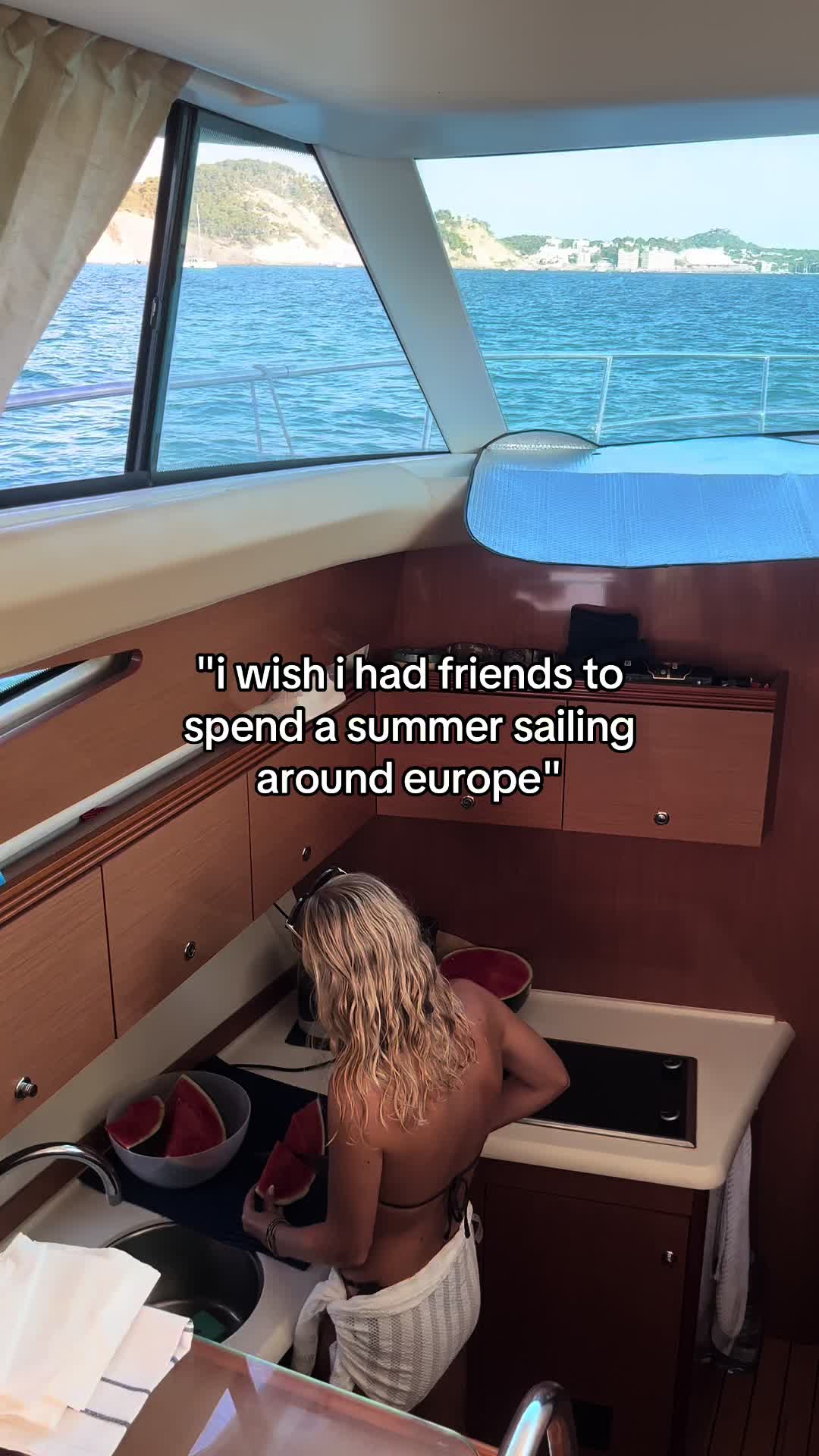 A woman is in a boat's cabin, seen from behind while preparing watermelon, and a text overlay that wishes for sailing friends.