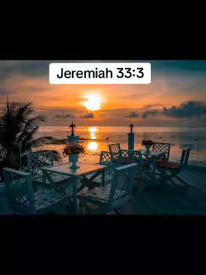 A serene sunset scene over a calm ocean with a deck set for dining in the foreground. A table and chairs are arranged, and the sun is in the middle of the shot at the horizon.
