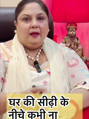 A woman with dark hair and a cream-colored scarf is speaking into a microphone. Behind her is a small statue. A text overlay at the bottom of the image is in a yellow box.