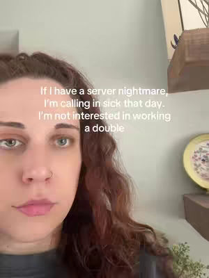 A woman with long, wavy reddish-brown hair is positioned in front of a light-colored wall. She looks slightly downcast, with text overlayed on the image. The woman is wearing a dark-colored top, and the background includes a glimpse of a shelf with decorative items, and a small plant.