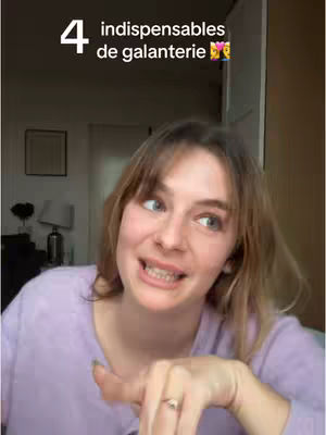 A woman with a slight smile looks towards the right side of the image and points to the ring on her finger. Overlay text in white states '4 indispensables de galanterie'. The background shows a home interior.