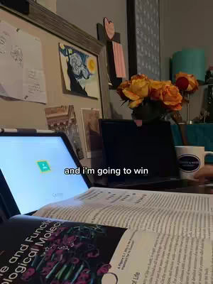 A desk with a laptop, open textbook, and a coffee cup, with a bouquet of orange roses on the right. The laptop screen displays a website with a logo. The text overlay reads "and I'm going to win."