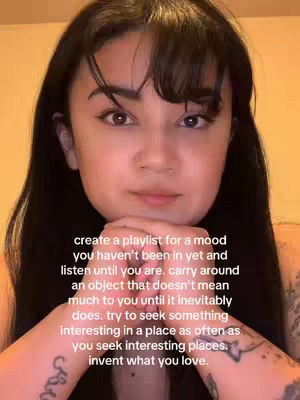 A selfie-style shot featuring a young woman with dark hair and a neutral expression. She is looking directly at the camera with her hands clasped gently in front of her face. The background appears to be a warm-toned wall. The overall composition is simple, focusing on the woman's face with overlayed text.