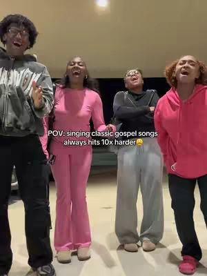 Four people are standing close together, facing the camera with their mouths open in song. They are standing in a lit area with neutral-colored walls and flooring. The group consists of individuals of diverse ethnicities, one wearing glasses. Text overlay stating 'POV: singing classic gospel songs always hits 10x harder' is visible.