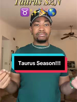 A man is centered in the frame, wearing a dark hat with colorful decorations on top. He is wearing a green shirt and a silver chain necklace. A text overlay reads 'Taurus Season!!!' A variety of emojis, including a Taurus symbol, are found at the top of the frame.