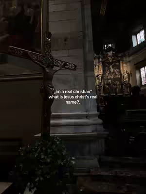 The image shows the interior of a church or cathedral with a crucifix in the foreground. The crucifix is made of dark wood, with a statue of Jesus Christ on it. In the background a religious altar can be seen near some windows.