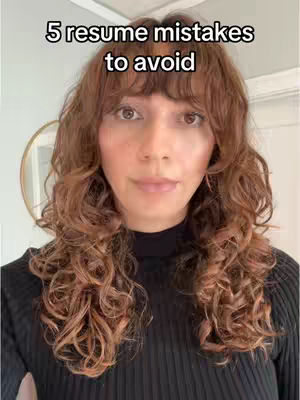A medium, near-framing shot features a woman with curly brown hair, her head angled slightly. Above her is text that states, '5 resume mistakes to avoid'. The background is a light and neutral color and shows partial view of an oval mirror.