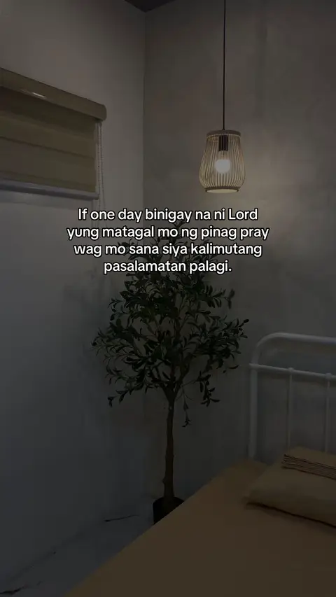 The image captures a dimly lit interior with a minimalist aesthetic. A hanging lamp with a wicker shade illuminates the space, casting soft light. A small, stylized tree in a black pot adds a touch of nature. Text appears on the image, overlayed diagonally reflecting the ambient lighting.