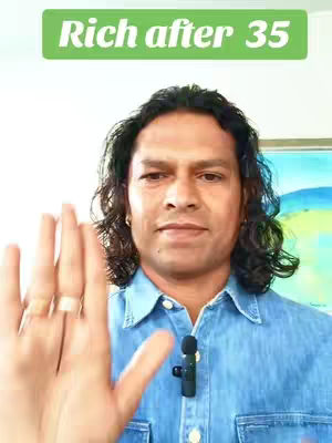 A man with long dark hair is in front of a colorful painting. The man is showing his palm. A green banner is floating in the air on top