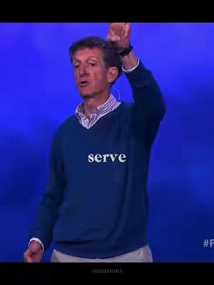 A man in a blue sweater is positioned center frame, raising his right hand. The background is a gradient of blue. The word "serve" is overlaid on his sweater.