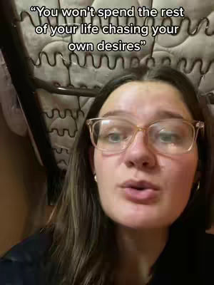 A woman with glasses is in close-up, set against a patterned background, likely a bed headboard. Text overlay states: "You won't spend the rest of your life chasing your own desires".