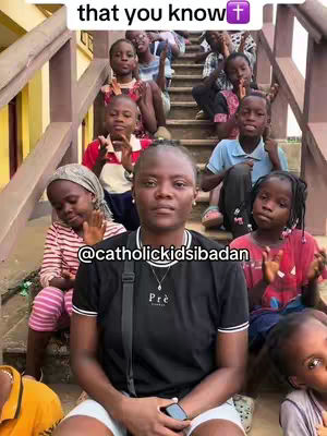 A woman sits centered at the bottom of a stone staircase and faces the camera. Several children sit on the staircase behind her. The woman wears a black t-shirt and holds a black phone. The children are of various ages and wear casual clothing.