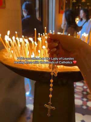 The image shows a close-up of a hand holding a rosary with a cross, with many burning candles in the background. The text overlay indicates a healing mass at Our Lady of Lourdes.