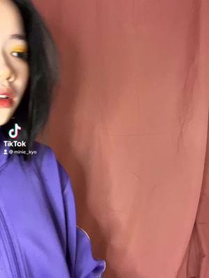 The cover image shows a close-up of a person's face, facing slightly left. The person has dark, short hair, and is wearing a purple top. They have red lipstick, and yellow eyeshadow, with the TikTok logo in the bottom left. The background is a solid reddish-brown color.