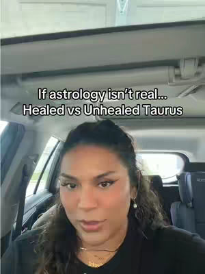 A woman is seated inside a car, facing the camera, with the interior visible in the background. Text overlays are present at the top of the video. The woman has dark curly hair and is wearing a black top and gold jewelry. The car's interior and the background are neutral colors.