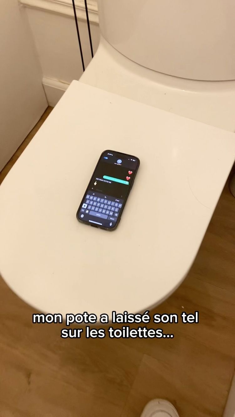A smartphone lies on a white toilet seat, displaying a messaging app with a partly visible conversation. Below, text reads 'mon pote a laissé son tel sur les toilettes...' indicating the phone belongs to a friend left behind.