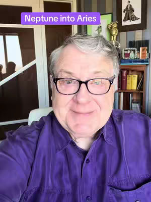 A man with glasses and a purple shirt smiles at the camera, with a purple rectangle overlaying the top of his head that reads, "Neptune into Aries."