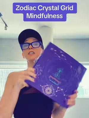 A person wearing glasses and a cap is holding a purple box with a diagram and symbols on it. The text overlay says 'Zodiac Crystal Grid Mindfulness'.