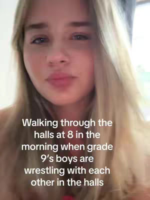 A selfie-style video shows a fair-skinned young woman with long blonde hair, with the top of her torso and head visible. She looks directly at the camera with a slight frown. Text overlays are added to the image.