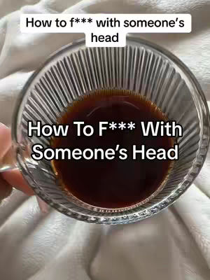 The image shows a clear glass with ribbed sides filled with a dark brown liquid, possibly coffee or tea, against a soft, white, possibly a blanket, backdrop. The text overlays read, "How to f*** with someone's head" and "How To F*** With Someone's Head."