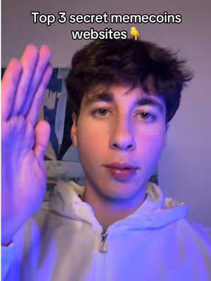 A young man is in the frame from the chest up, facing the camera. He has dark hair and is wearing a white hoodie. Above him, text reads, 'Top 3 secret memecoins websites'. His left hand is raised towards the top left corner. The background is out of focus, with a hint of a wall with some artwork. The lighting is soft and seems to come from the left side.